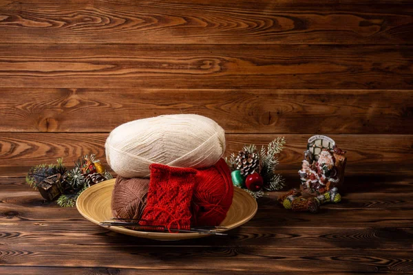 colored balls of thread, knitting needles and Christmas toys on wooden background