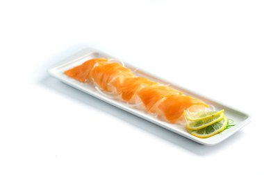 izole beyaz arka planda dikdörtgen bir plaka üzerinde limon ve otlar ile kırmızı balık parçaları