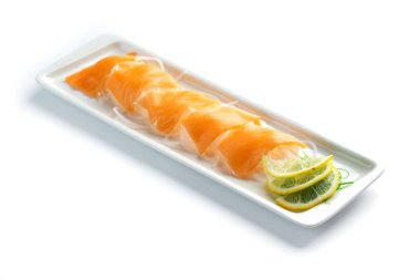 izole beyaz arka planda dikdörtgen bir plaka üzerinde limon ve otlar ile kırmızı balık parçaları