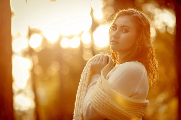 red-haired girl in light clothes against the backdrop of the autumn forest against sunlight