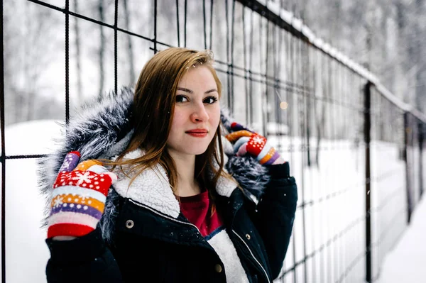 La chica al lado de la cerca de barras de metal en medio del bosque de invierno —  Fotos de Stock