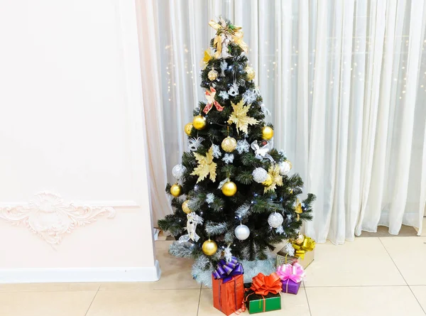 Weihnachtsbaum geschmückt mit Spielzeug mit Geschenken in Schachteln darunter auf hellem Hintergrund — Stockfoto