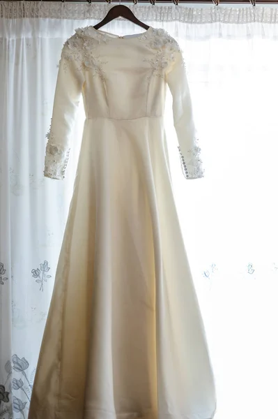 Robe de demoiselle d'honneur suspendue sur un cintre sur le fond d'une fenêtre avec un rideau blanc — Photo