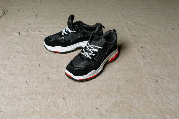 Black sneakers on thick white with red accents soles on a gray concrete background — Stock Photo, Image