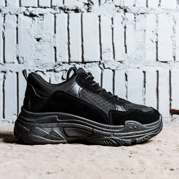 Black sneaker with thick soles on the cement floor against the background of brick wall — Stock Photo, Image