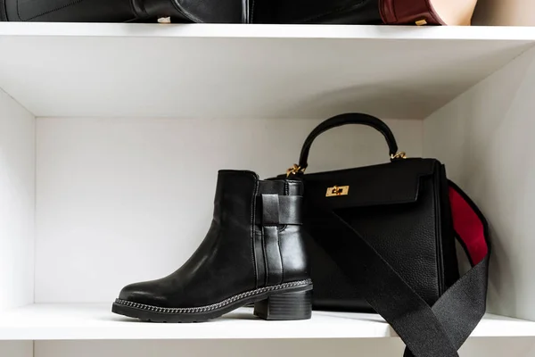 Par de zapatos de cuero negro con tacones bajos y un bolso negro con una hebilla de oro y un cinturón rojo en un estante blanco en la tienda — Foto de Stock