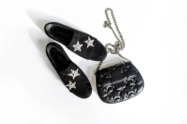 black suede shoes with a rhinestone star decoration and a black clutch on a chain with stars on a white background