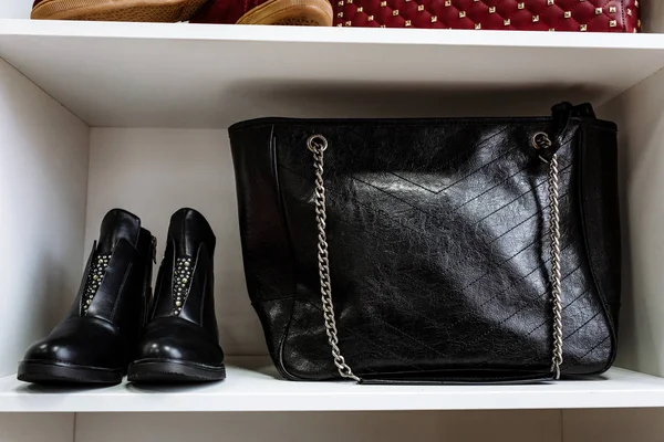Scarpe in pelle nera decorate con strass e una borsa in pelle nera su una catena su uno scaffale bianco nel negozio — Foto Stock