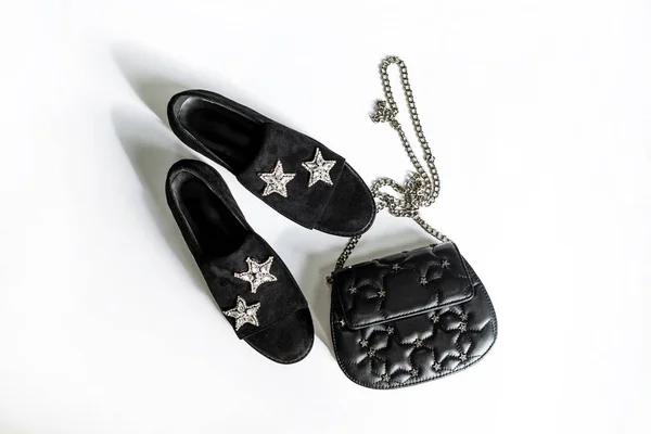 black suede shoes with a rhinestone star decoration and a black clutch on a chain with stars on a white background