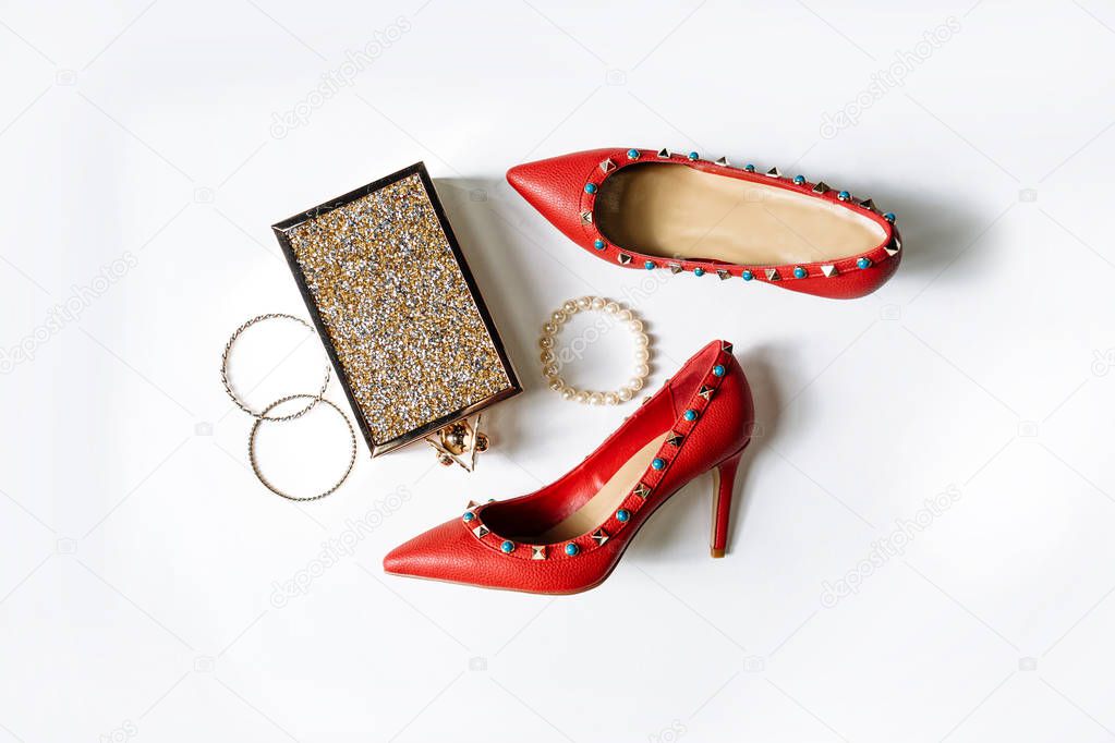 pair of red high-heeled shoes with pointed toes, decorated with metal blue inserts and metal clutch with sparcles on a white background