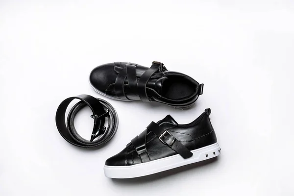 Schwarze Lederturnschuhe mit Riemen und weißer Sohle und schwarzem Ledergürtel auf weißem Hintergrund — Stockfoto