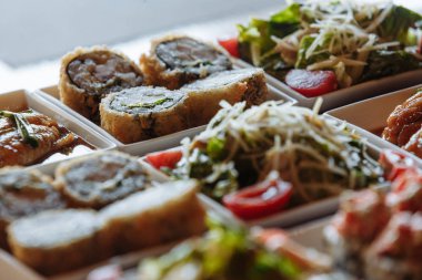 Masanın arka planında ahşap standlar üzerinde beyaz kare tabaklarda çeşitli Japon yemekleri