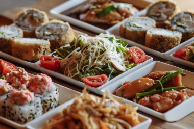 Masanın arka planında ahşap standlar üzerinde beyaz kare tabaklarda çeşitli Japon yemekleri