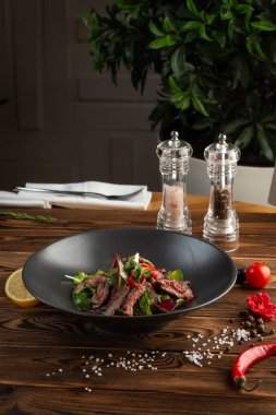 Ahşap arka plan üzerinde siyah tabak tay sığır salatası