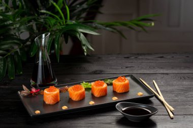 Siyah ahşap arka plan üzerinde siyah bir tabak üzerinde ton balığı ile ayarlanmış suşi rulo