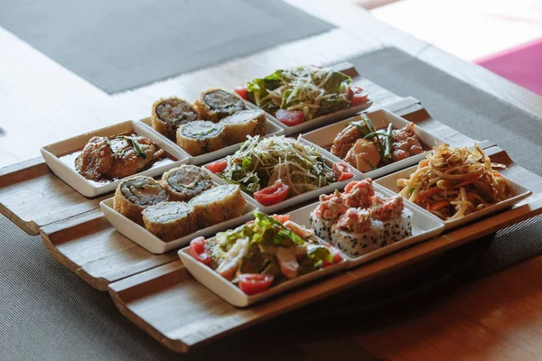 Różne dania kuchni japońskiej w białych kwadratowych płyt na drewnianych stoiskach na tle stołu — Zdjęcie stockowe