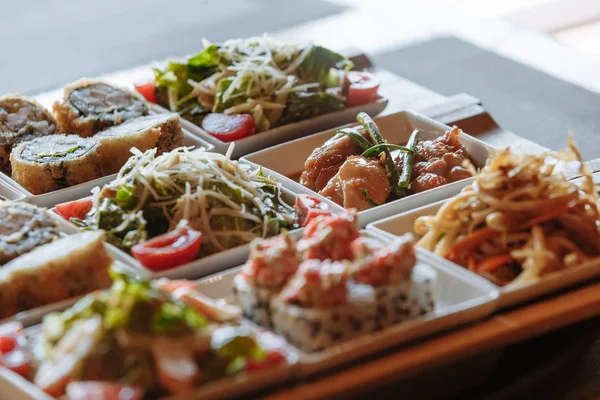 Masanın arka planında ahşap standlar üzerinde beyaz kare tabaklarda çeşitli Japon yemekleri