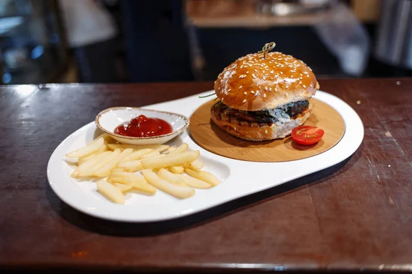 Hamburger zdobione pomidory, frytki i sos pomidorowy w owalnym talerzu na drewnianym stole — Zdjęcie stockowe