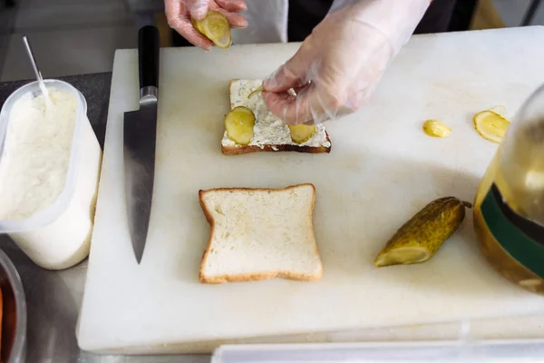 Повар в полиэтиленовых перчатках делает сэндвич на белой доске — стоковое фото
