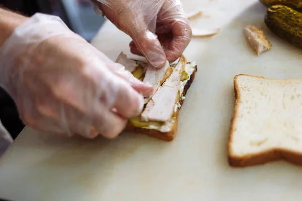 Готувати в поліетиленових рукавичках, роблячи бутерброд на білій дошці — стокове фото