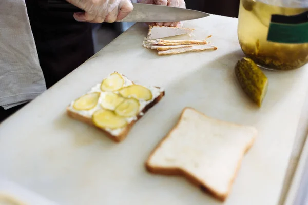Готувати в поліетиленових рукавичках, роблячи бутерброд на білій дошці — стокове фото