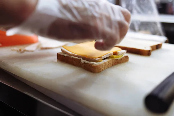 Повар в полиэтиленовых перчатках делает сэндвич на белой доске — стоковое фото
