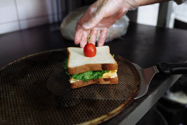 Koch in Polyethylen-Handschuhen, der ein Sandwich auf einem weißen Brett zubereitet — Stockfoto