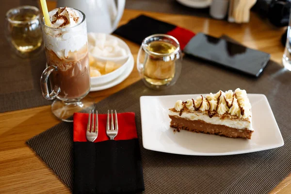 Un pedazo de pastel, un batido en un vaso, una tetera, tazas de té y cubiertos en una mesa en un café — Foto de Stock