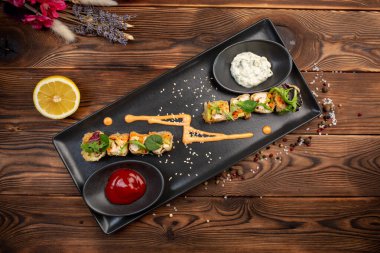 Siyah dikdörtgen bir tabakta yeşillikle süslenmiş ruloları hamura yerleştir.