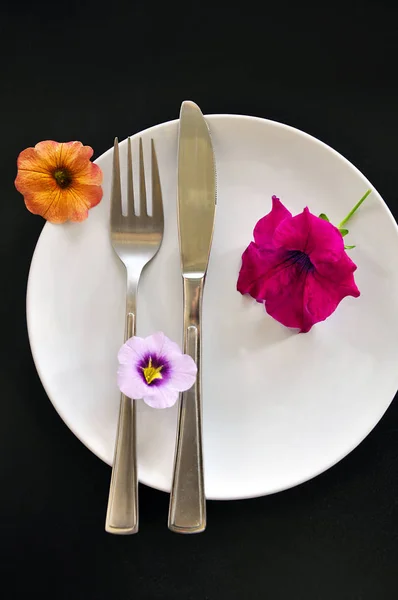 Beyaz plaka üzerinde çatal bıçak takımı ile parlak petunya çiçekler