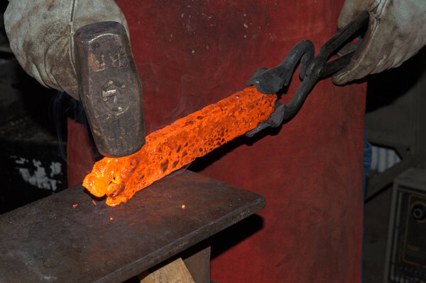 Red hot from the intense heat of a forge, the blacksmith skillfully works the glowing metal to contour it into a handmade knife.