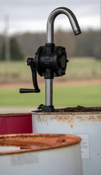 A defocused foreground and background draws the eye to the hand crank pump on the rusty barrel of old oil.