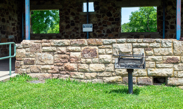 Вид на лес через открытые окна в каменном приюте для пикников в лагере Eucha Oklahoma с бесплатным грилем из древесного угля и зеленой травой.