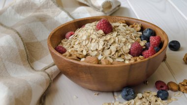 siyah ahşap bir masa üzerinde ahşap bir kapta yaban mersini, ahududu, badem ve ceviz ile yulaf ezmesi