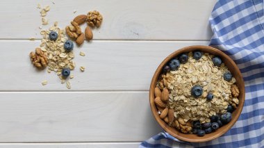 siyah ahşap bir masa üzerinde ahşap bir kapta yaban mersini, badem ve ceviz ile yulaf ezmesi