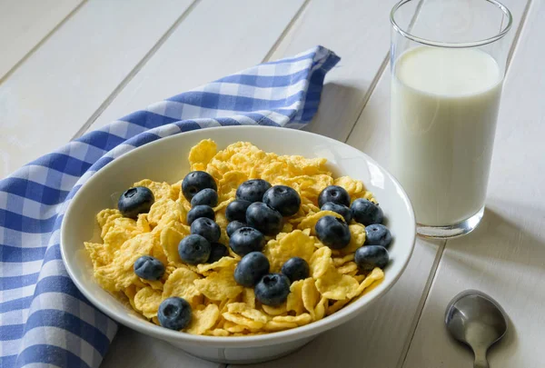 Morning breakfast. Plate of cornflakes with blueberries and a glass of milk on a light wooden background