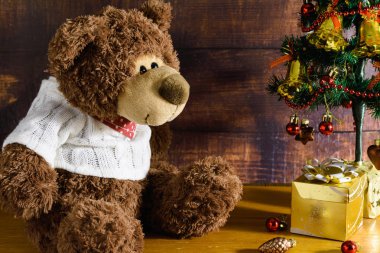 Oyuncak masada. Oyuncak ayı, bir Noel ağacı ve hediye kutusunun yanında kahverengi bir arka planda, ahşap bir masada oturuyor.