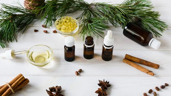 Composición de aceites naturales, botellas de vidrio con aceite, varillas de canela, anís, piñones sobre una mesa de madera blanca sobre un fondo de ramas verdes. vista superior — Foto de Stock