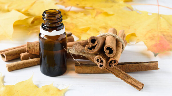 close-up, cinnamon sticks and cinnamon oil on a white wooden background