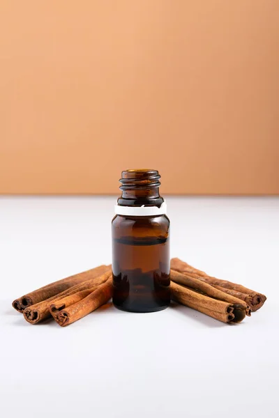 Composition with essential cinnamon oil in glass bottle on white background