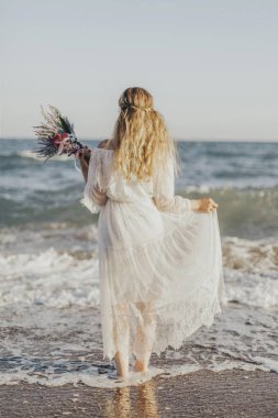 Deniz ve elinde çiçekler ayakta gelin