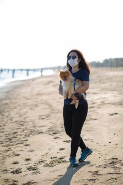 Genç bir kadın köpeğiyle kumsalda güneşleniyor.