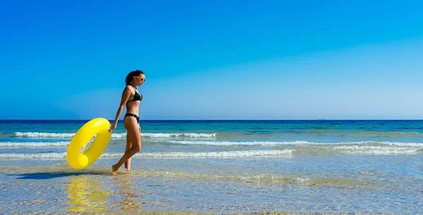 Vakantie vrouw in bikini met gele praalwagen wandelend langs de zee — Stockfoto