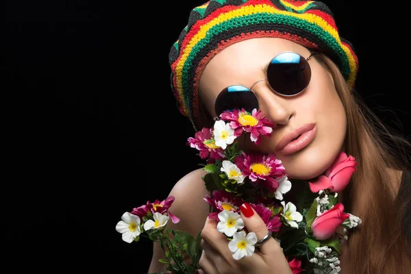 Jeune femme en lunettes de soleil et chapeau rasta tenant des fleurs — Photo