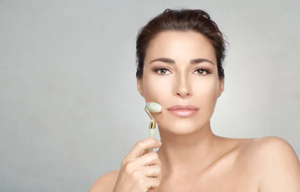 Attractive woman using face roller on cheek. Skin care and beaut