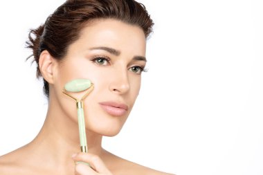 Woman using jade face roller on her flawless skin. Facial treatm clipart