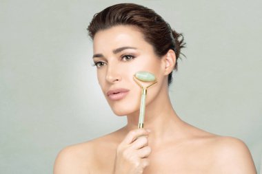 Woman using jade roller on her flawless skin. Facial treatments  clipart