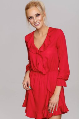 Kırmızı elbiseli gri arka plan üzerinde poz gülümseyen güzel sarışın kadın