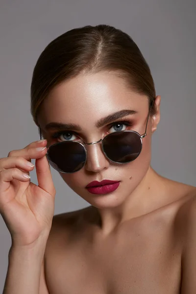 Портрет молодой девушки носить солнцезащитные очки изолированы над серым — стоковое фото