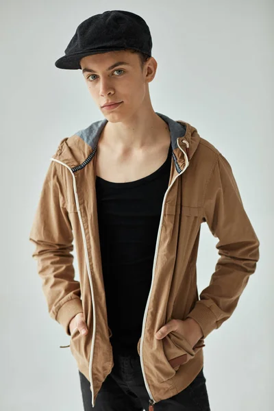 Handsome teen in beige jacket and black cap posing in studio